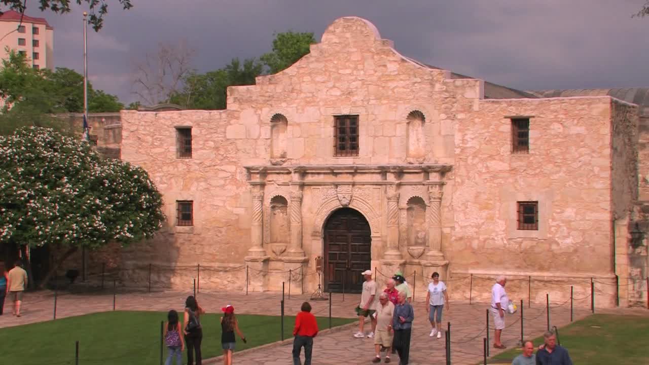 사람들은 샌안토니오 텍사스 1에 있는 돌 안뜰과 건물을 돌아다닙니다.