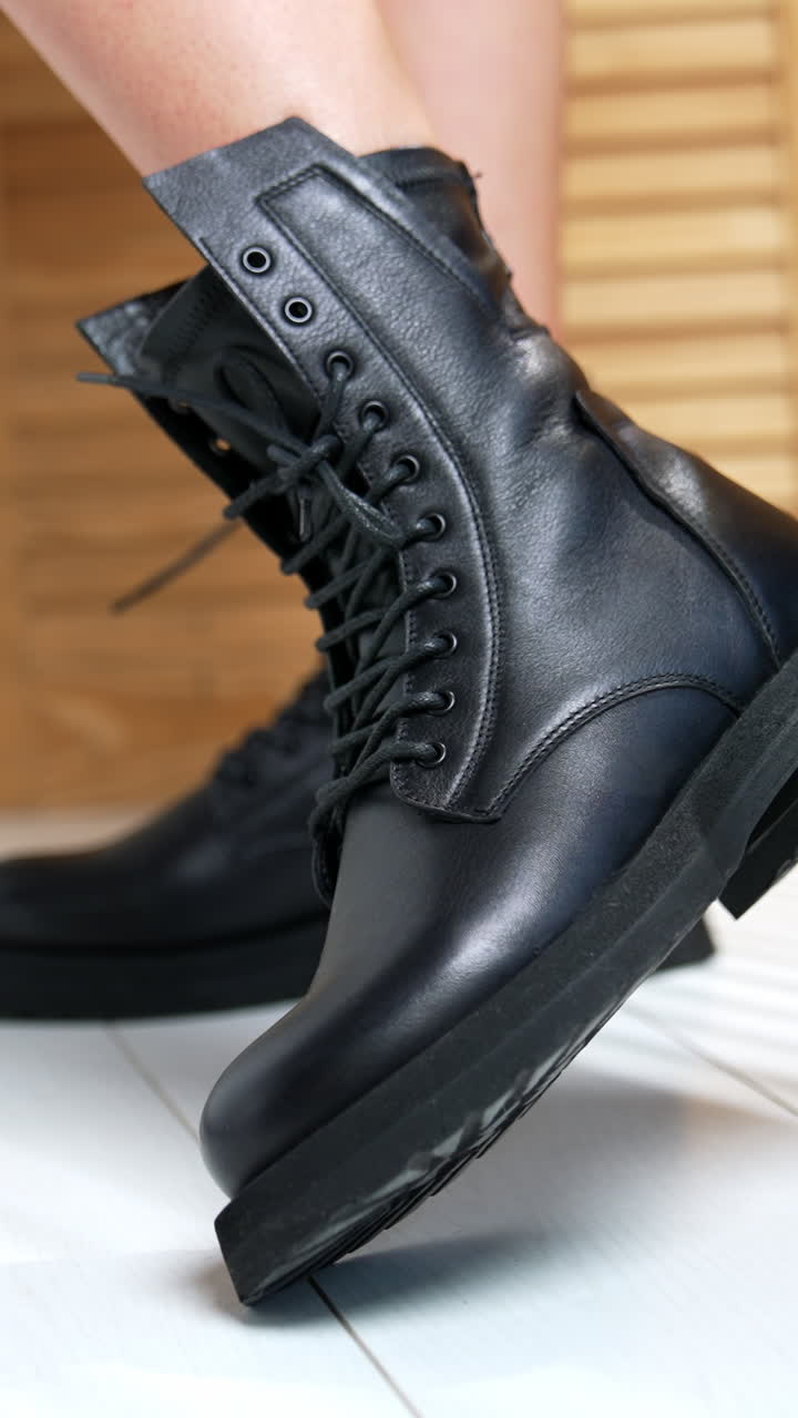 Demonstration of stylish army boots with laces on female feet. Woman moving her feet in fashionable footwear in front of camera. Close up. Wooden screen at backdrop. Vertical video