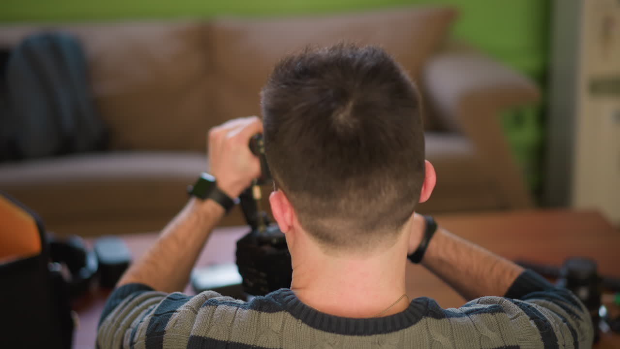 Man adjusting video camera on tripod in home studio, focused on equipment setup. Green walls and modern furniture in background, preparing for filming or content creation with soft lighting