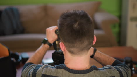 man adjusting video camera on tripod in home studio, focused on equipment setup. green walls and modern furniture in background, preparing for filming or content creation with soft lighting