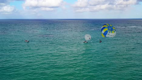 two people parasailing together in yellow and blue parachute in open green ocean waters, circle aerial