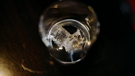 dropping ice cubes in the glass with black background, top down view