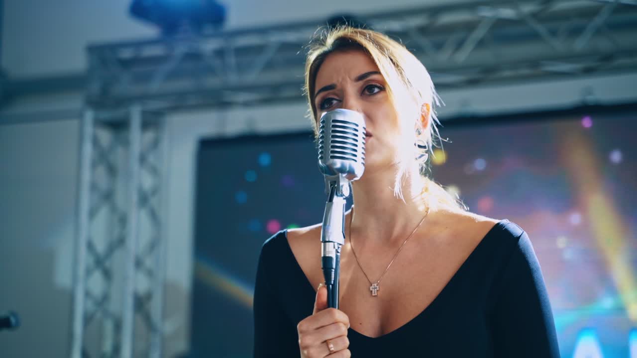 Woman singer on the stage. Beautiful girl performing a song into the microphone on the background of video on stage.