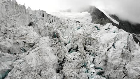 aerial flyover through the crevasses of the moiry glacier near grimentz in valais, switzerland with a pan down view from the mountain peaks to the ice on a cloudy summer afternoon