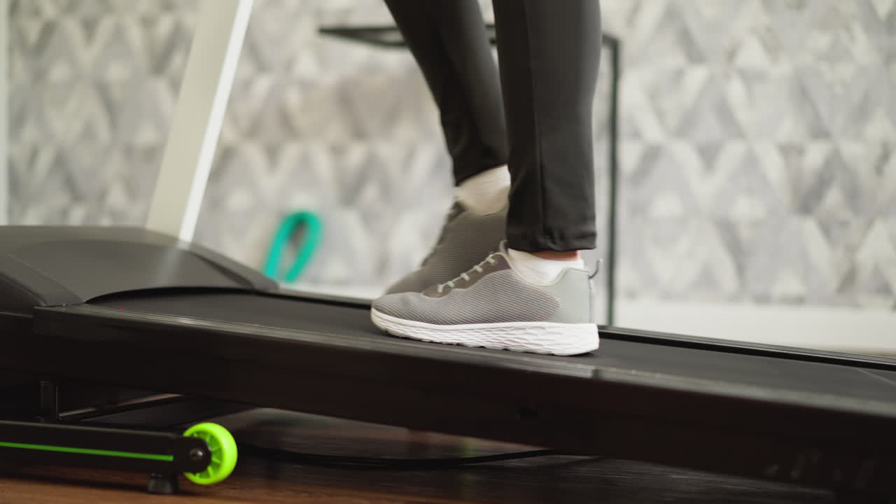 Woman walks and runs on treadmill at home closeup. Sportive lady with slim legs exercises on automatic trainer in domestic gym. Fitness training