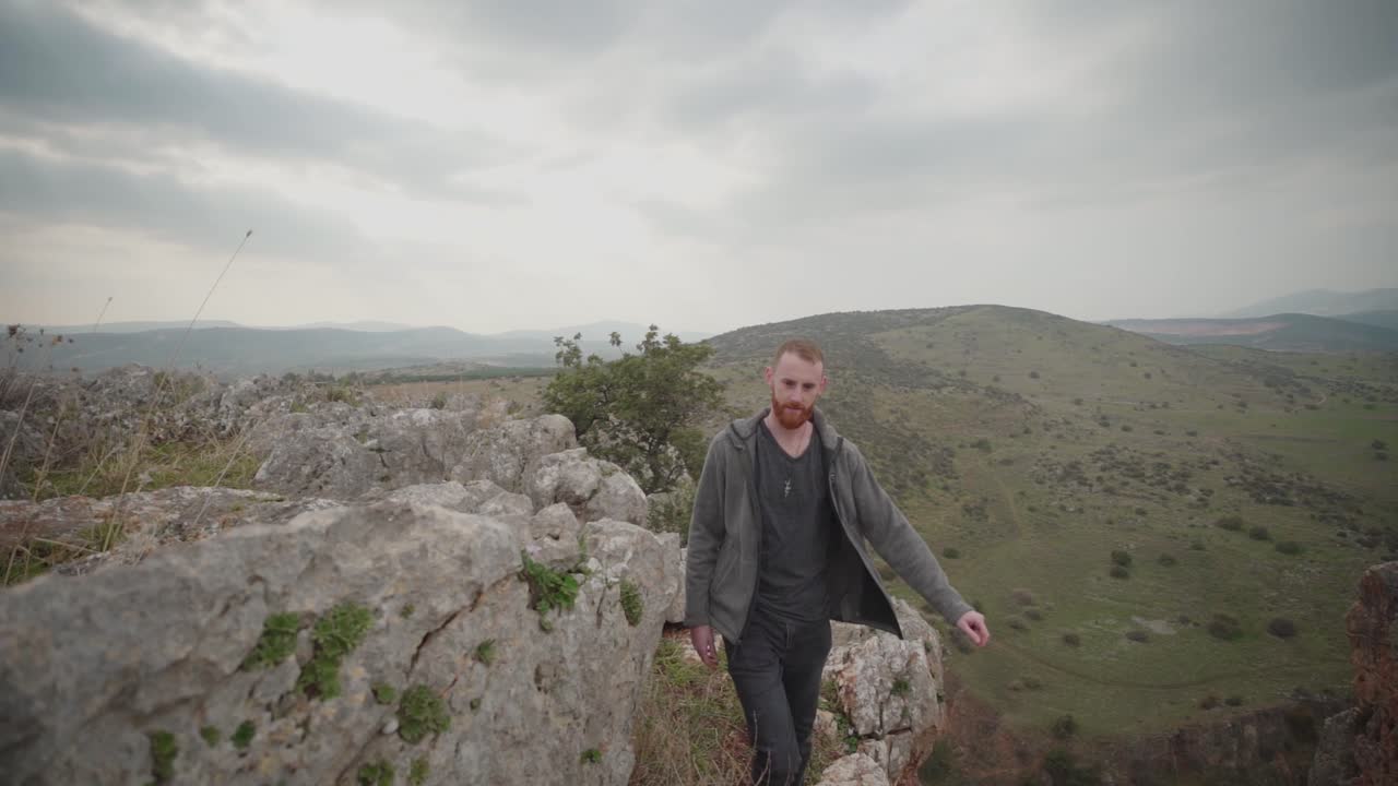 hombre pelirrojo con barba caminando a lo largo del borde del acantilado rocoso, israel, caminando hacia la cámara