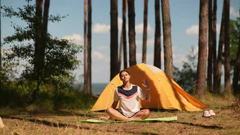woman practicing yoga in a forest near a tent