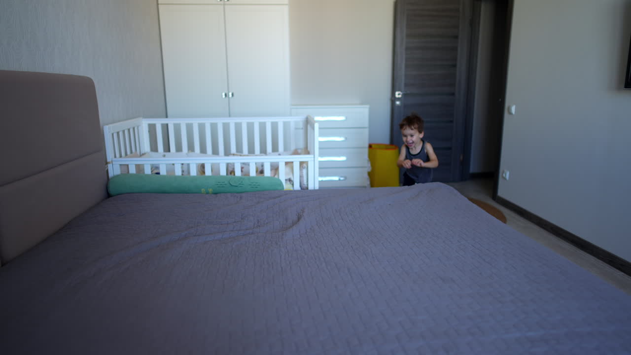 Adorable smiling toddler kid gets on the large bed. Cute active baby boy starts jumping on the bed.