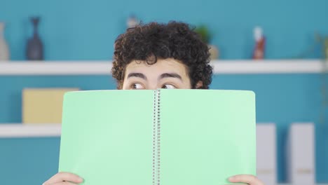 glücklicher männlicher student schaut in die kamera, während er ein buch in der hand hält.