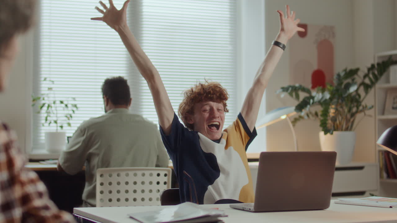 Young Man Using Laptop and Celebrating Success at Work in Modern Office