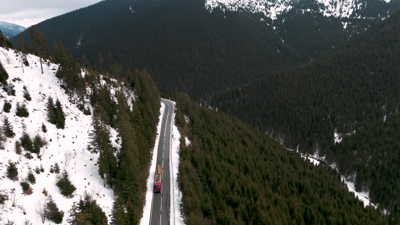 vuelo aéreo de un camión cargado con madera conduciendo a través de las montañas y bosques cubiertos de nieve en una carretera en transilvania rumania europa 2023 - transporte de madera - vista de pájaro