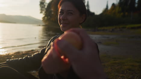 woman gives orange to partner. positive emotions from spending time together near lake. lovers enjoying untouched nature at sunset twilight in autumn evening