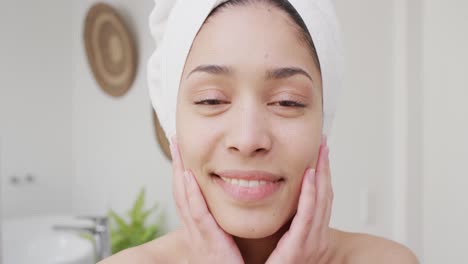 retrato de una mujer biracial con una toalla sonriendo en el baño