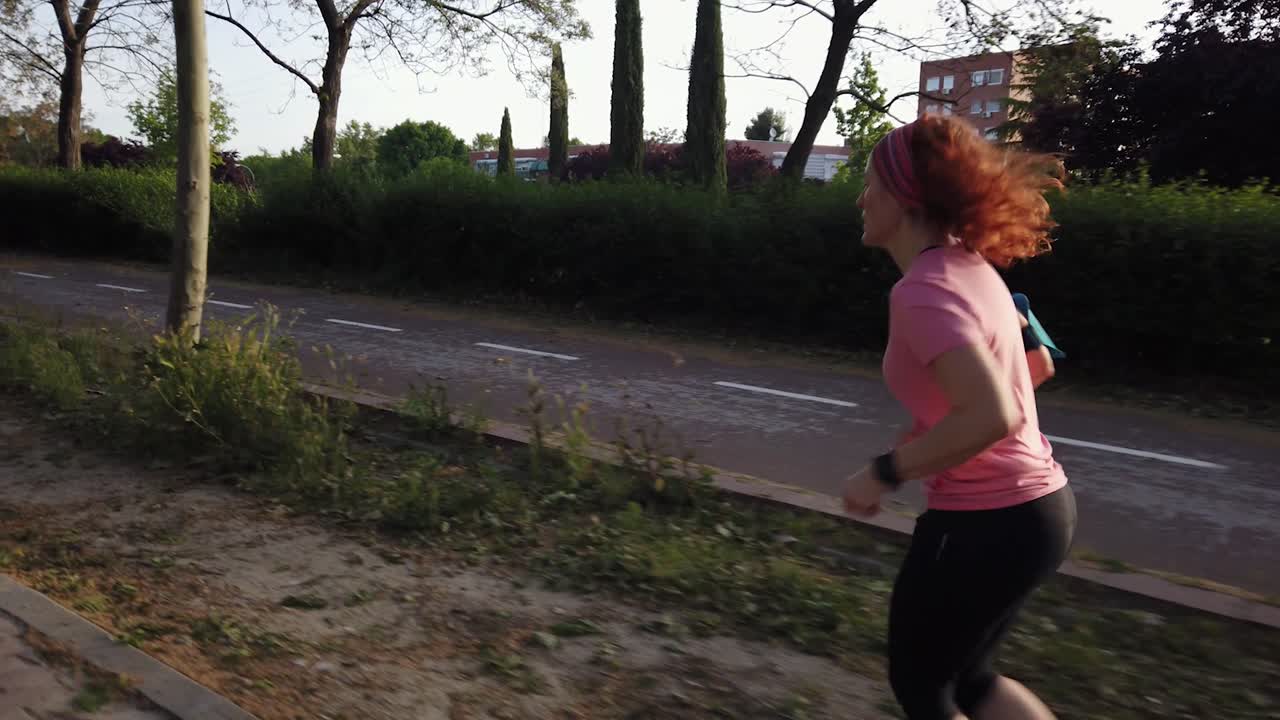 A side shot following a woman as she runs beside a bike lane in a park.