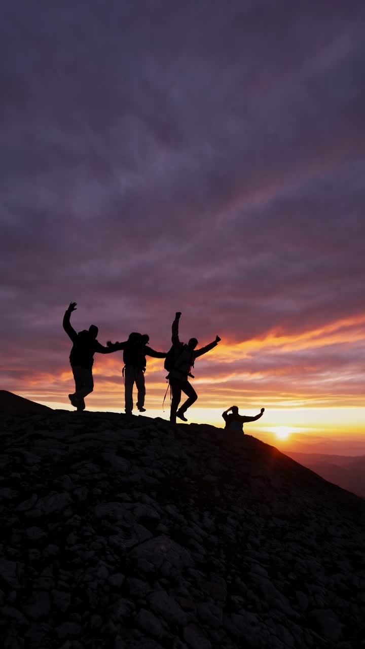 Silhouetted hikers ascend a rocky hill at sunset, captured from a low angle