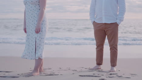 barefoot couple on sandy shore with gentle waves, soft sunset light