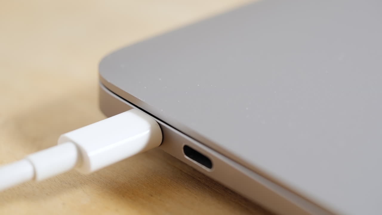 primer plano, desenchufando el cable usb-c de la computadora portátil plateada en un escritorio