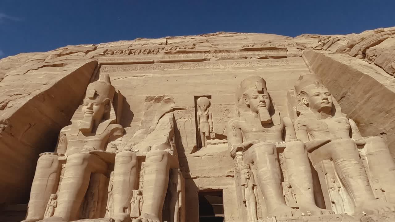 A majestic front view of the Great Temple at Abu Simbel, showcasing the colossal seated statues of Pharaoh Ramesses II carved into the sandstone cliffs. This UNESCO World Heritage site.