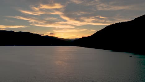 golden sunset cloudscape over a mountain lake in silhouette - sliding aerial hyper lapse