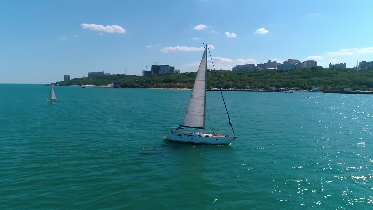 Young women relaxing on a white yacht. Luxury sailboat floating on the sea water on the city background. Sea voyage in summer day. Camera rising.