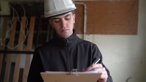 professional architect in white hard hat writing down plan details of a house for improvement