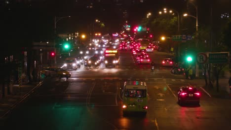 busy street traffic at night in taipei with traffic lights turning red to green while a bus crosses the avenue from left to right – wide shot