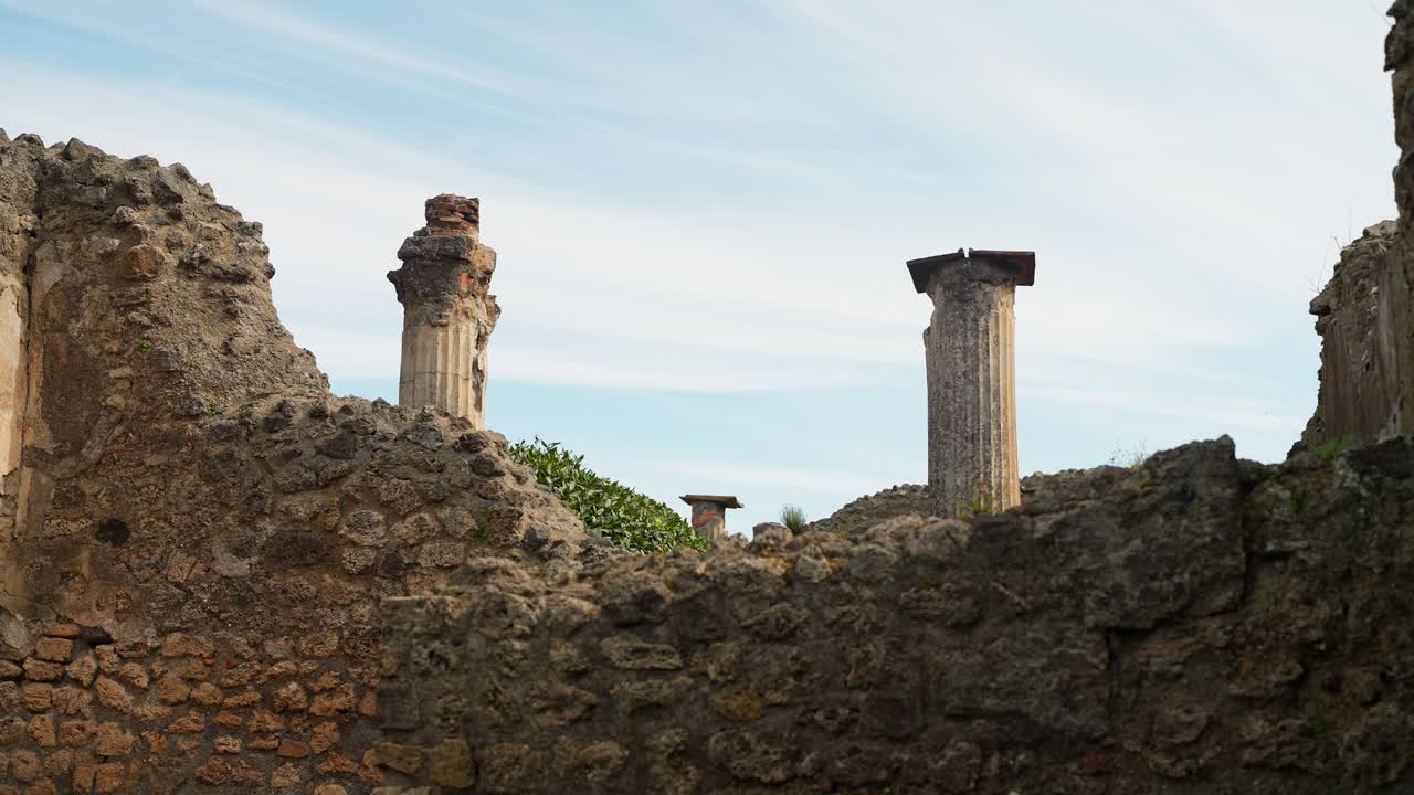 Vista sulle mura di Pompei erose dal tempo con colonne romane superstiti che si ergono contro il cielo, evidenziando i resti esposti di un antico complesso architettonico in Italia