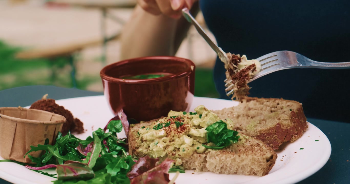 Ein Teller mit einer gesunden Mahlzeit, mit Händen, die Tafelmesser und Gabel halten, Brot, Gemüse und Saucen, vegetarischer Lebensstil, Essen im Freien, Nahaufnahme