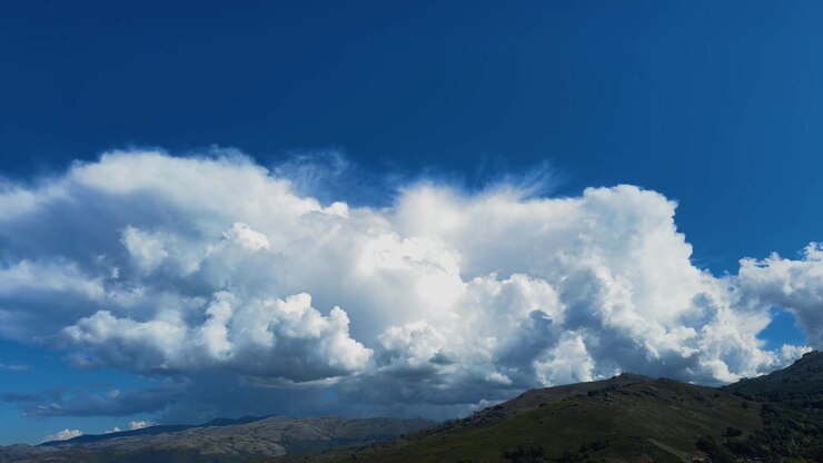 massive white cumulus clouds building up rapidly like an explosion over a mountain ridge against a deep blue sky.