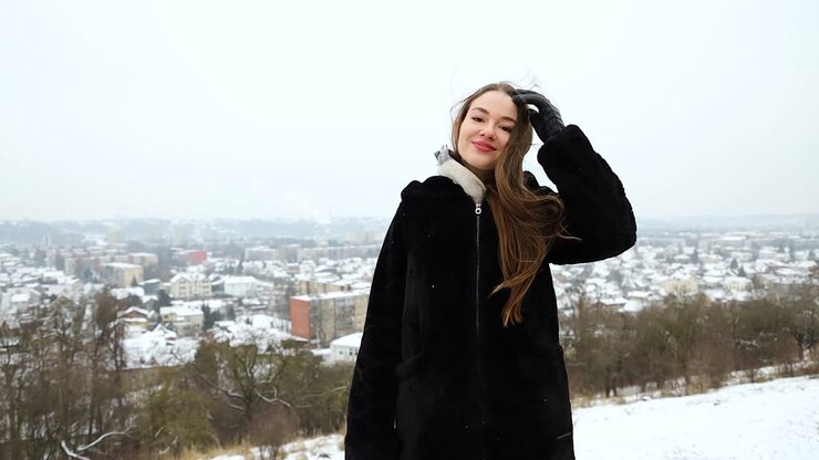 Modella felice in posa in cima a una montagna di fronte a una città in una bella giornata invernale.
