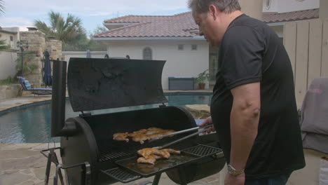 tilt down to bbq chicken thighs being put on to hot grill in back yard with pool