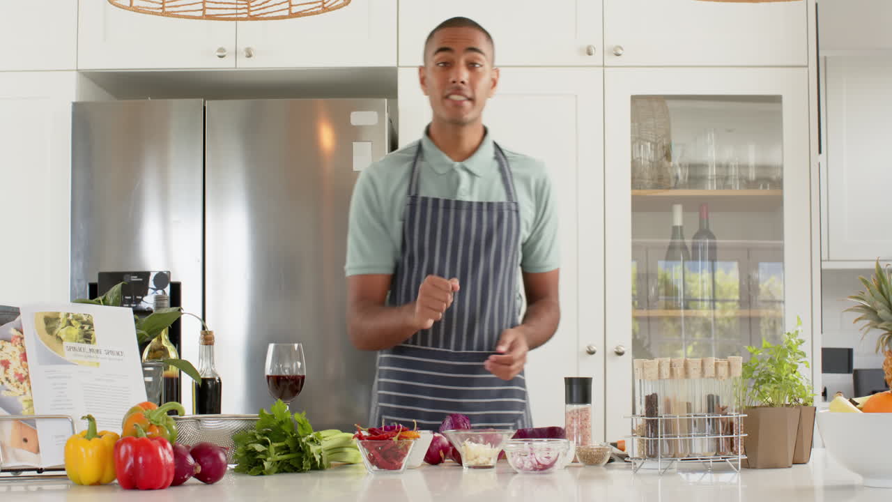 vlogger de cocina masculino biracial en delantal hablando y filmando en la cocina