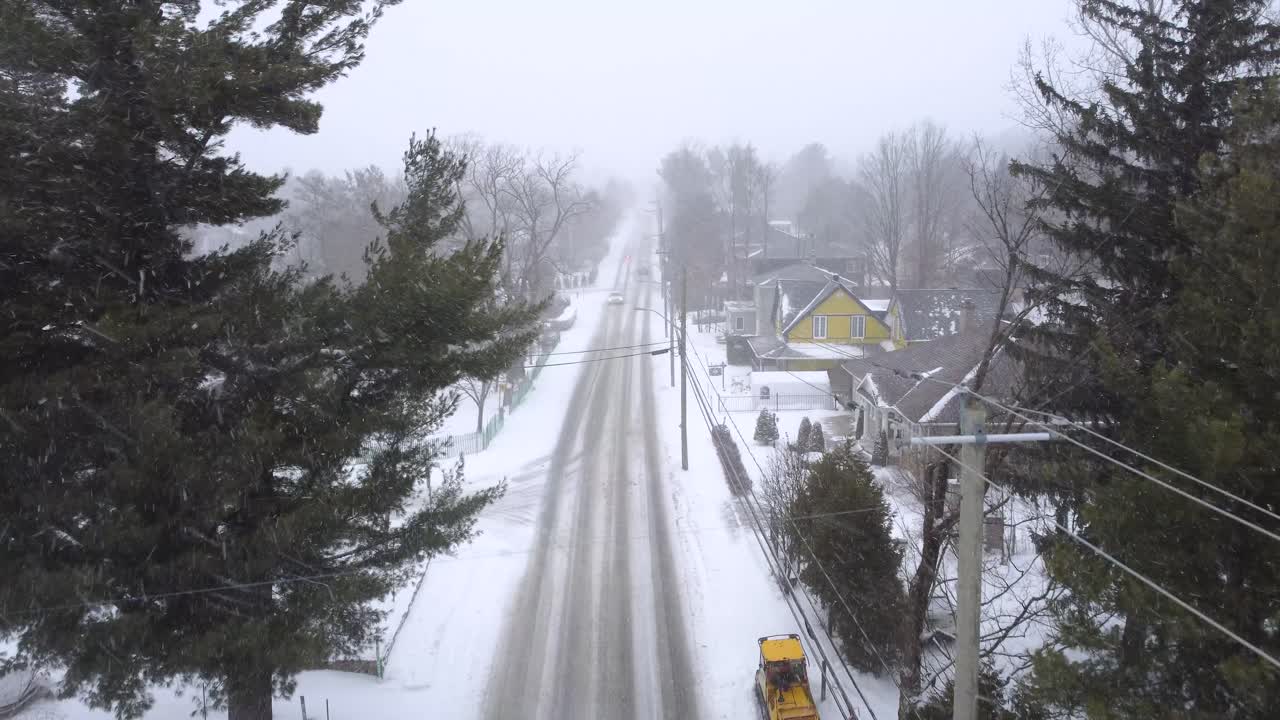 Drone rising above cars and snow plow clearing road in a winter storm