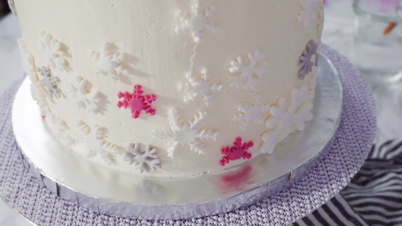 Decorating round funfetti cake with pink and white fondant snowflakes.