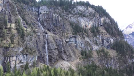 Drone-flight-over-a-beautiful-alpine-valley,-waterfalls-and-high-snow-capped-mountains