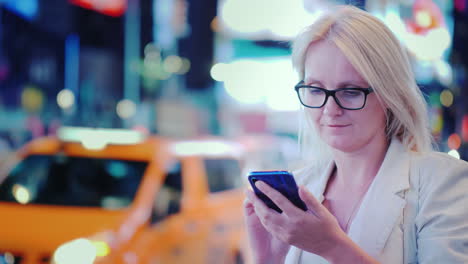 una mujer joven usa un teléfono inteligente en una calle concurrida en manhattan contra el telón de fondo de publicidad brillante