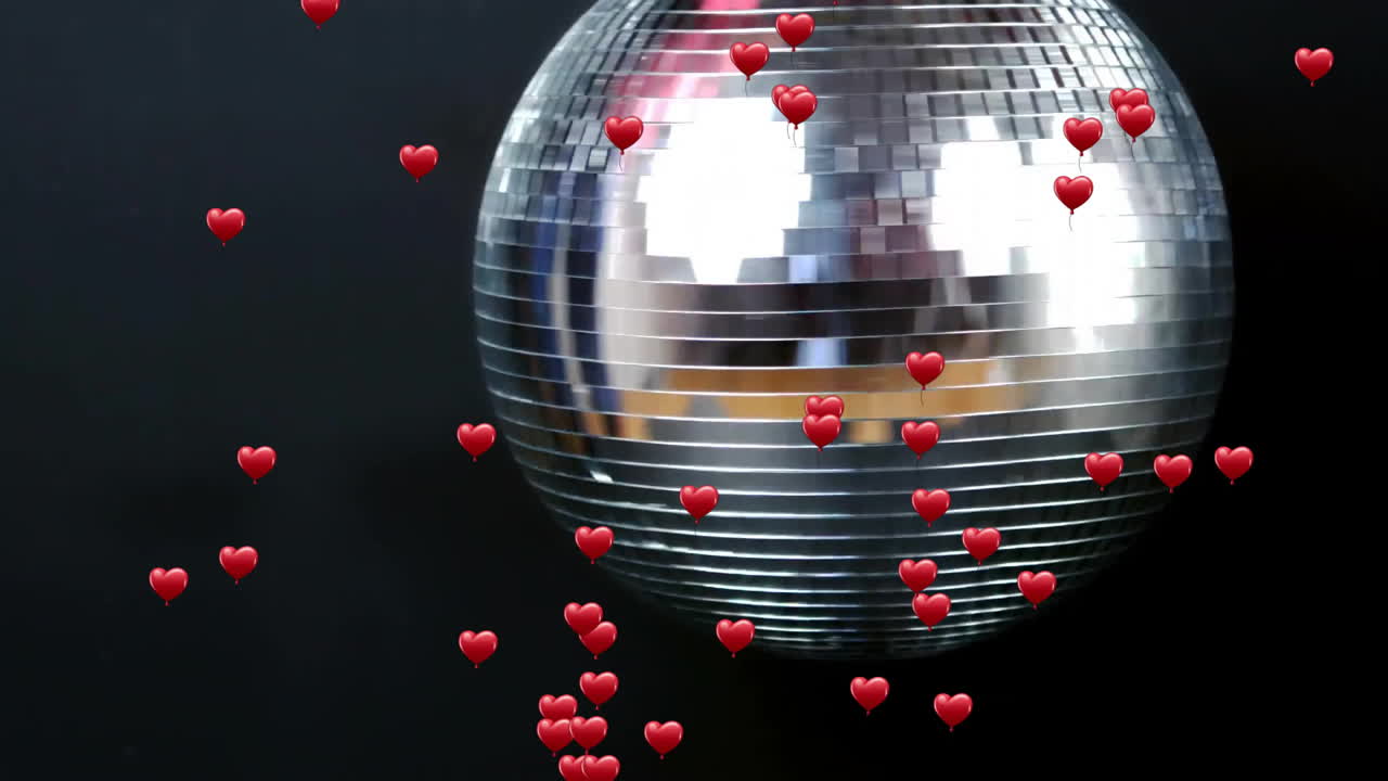 Mirrored disco ball shining on dark background, reflecting numerous floating red heart emojis