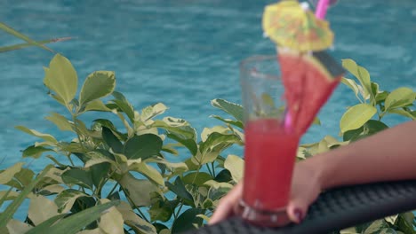 woman on lounge chair holds glass with drink near blue pool