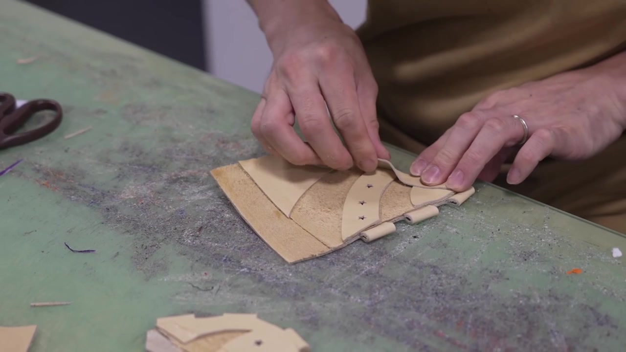 Hands folding and pleating small leather pieces while assembling parts of a baseball glove
