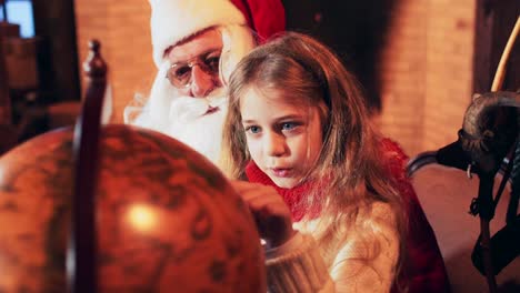 a girl sits on the hands of santa claus and turns an old globe. santa's christmas residence