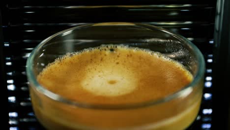 closeup view of a coffee drop dripping on the glass of frothy espresso - slowmo
