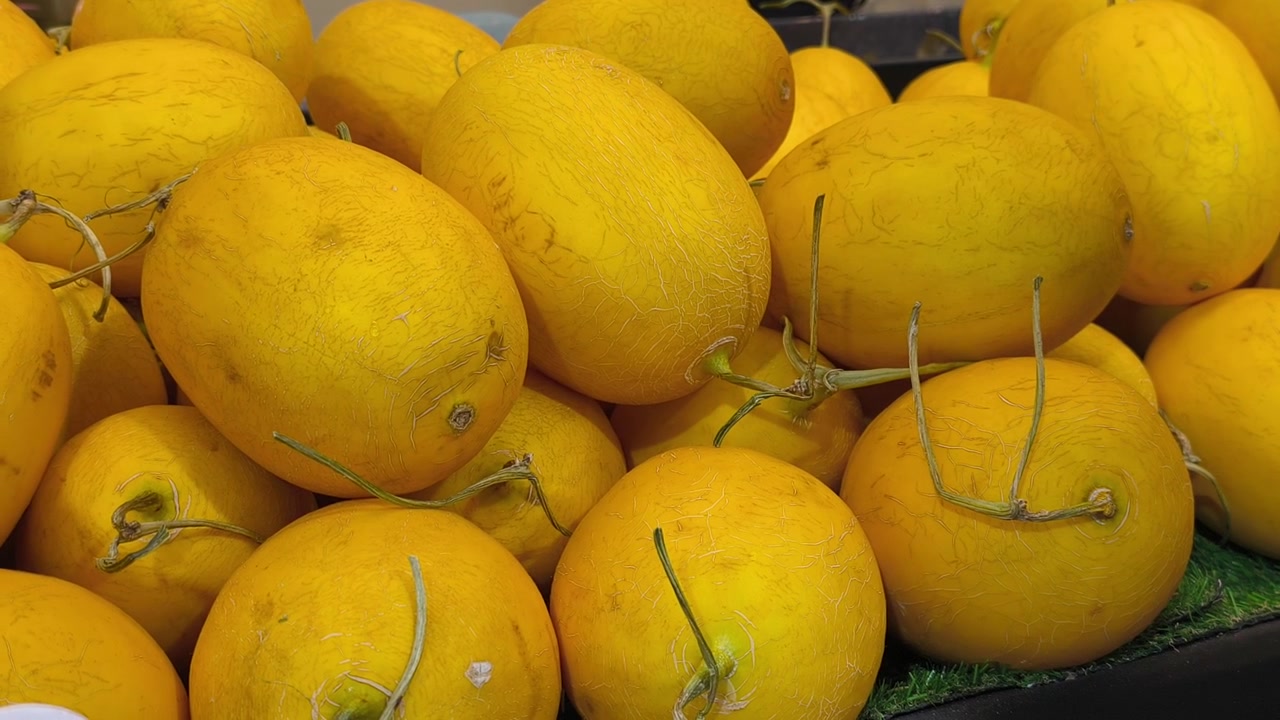 Fresh canary melons are piled neatly on a table for display. These bright yellow fruits are ready for sale at a local market.