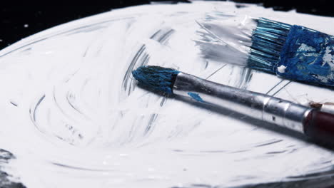 three wet paintbrushes jostled on white paint swirl