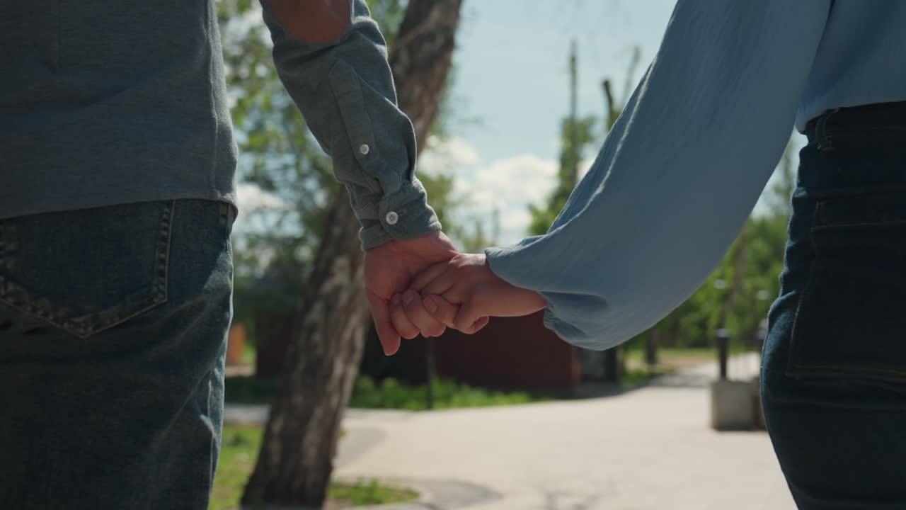 Pareja caminando de la mano al aire libre; amantes paseando por el parque de la mano; pareja caucásica disfrutando de un paseo con un toque delicado; primer plano de una pareja entrelazando los dedos durante un tranquilo paseo por el parque