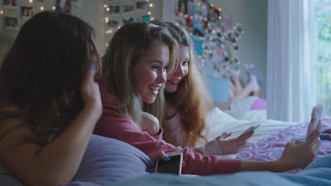 happy-teenage-girls-taking-selfie-photos-using-smartphone-best-friends-hanging-out-at-home-lying-on-bed-enjoying-weekend-together