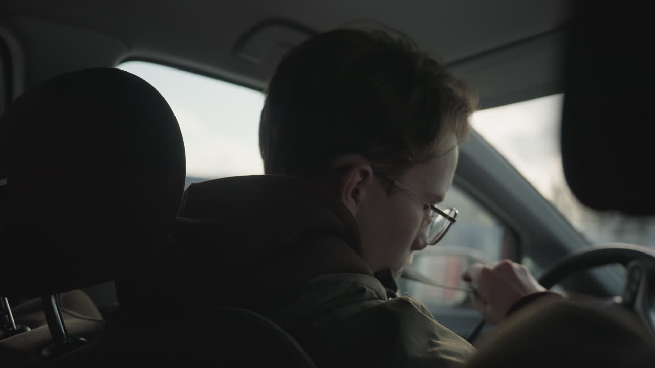 side view of young boy inside parked car fastening seatbelt with focused expression, dressed in hoodie and jacket, natural daylight entering through window