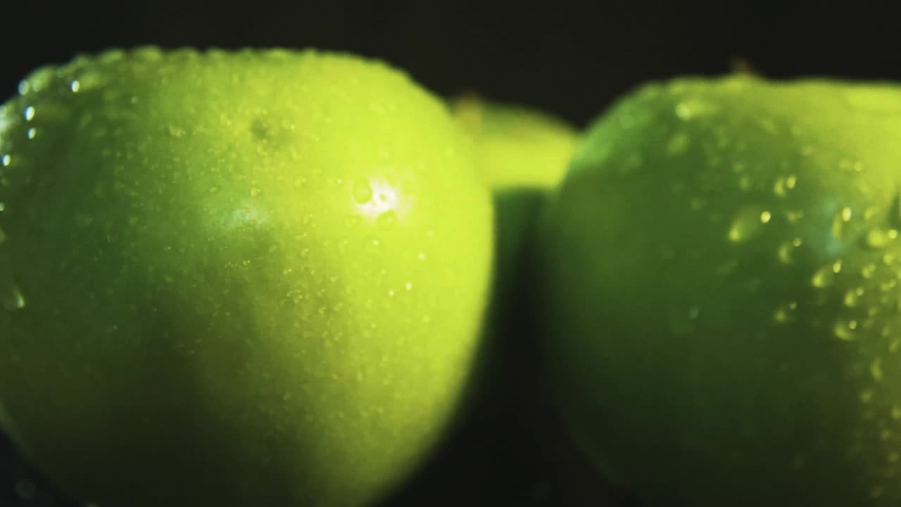 fotografía macro de manzanas verdes frescas giratorias con iluminación de gotas de agua en fondo negro y profesional