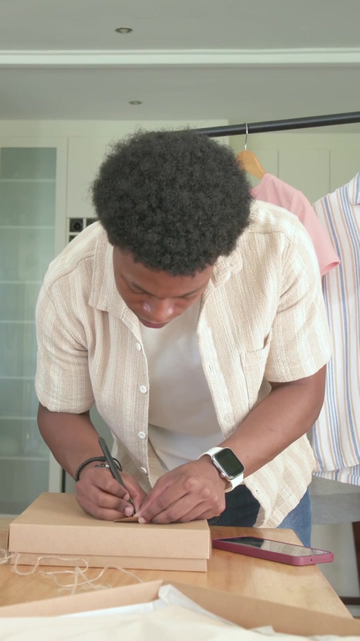 Vertical video: Opening box, man in beige shirt tying twine and wood tag to present gift at home