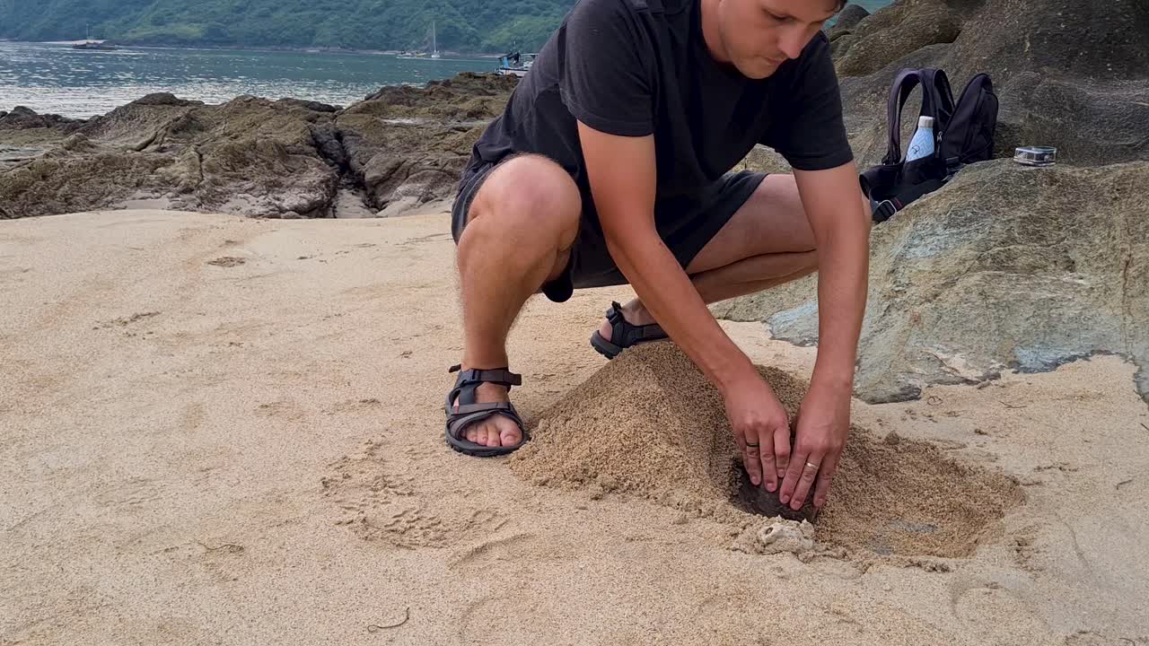 Man Digging and creating a Small Grave for a Deceased Pet on the Beach