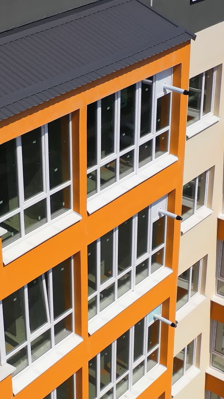 New urban multi storey building. Grey roof and bright orange walls with large balconies of a modern apartment building. Motion camera top down. Vertical video